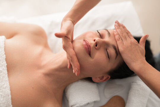 Relaxed young woman smiling while lying on table during face massage