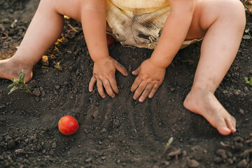 Close-up portrait of baby's hands digging in the ground, playing outdoors on spring day. Baby child wearing yellow summer suit. Portrait of happy girl.