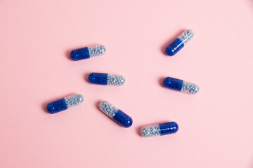 Pattern of blue pills on pink paper background with copy space, flat lay. Vitamins in tablet form.