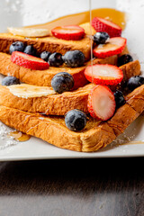 French toast. Brioche toast fried in butter and served with strawberries, blackberries, whipped cream powdered sugar and maple syrup. Classic American restaurant breakfast or brunch favorite.