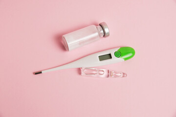 Electronic thermometer and ampoules on pink paper background with copy space, flatlay