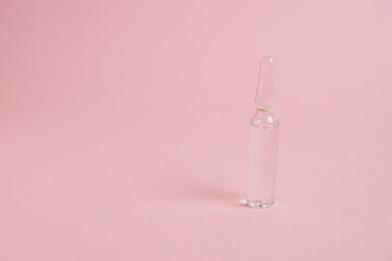 Transparent ampoule with medicine or vitamins on pink paper background with copy space