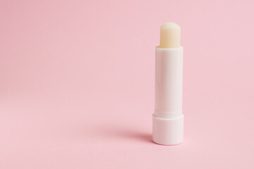 Transparent sanitary lipstick on pink paper background with copy space