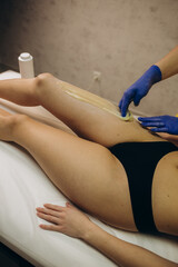 Woman having hair removal procedure on leg with sugaring paste in salon