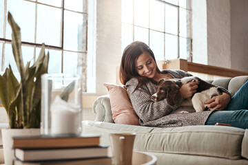 Woman relax on couch with puppy, happy and content at home with pet, happiness together with peace in living room. .Female cuddle dog, love for animals with smile and care, stress relief and comfort - obrazy, fototapety, plakaty