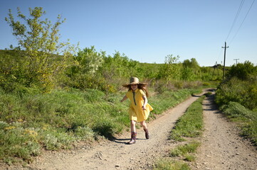 A teenage girl walks along the shore. A happy young woman in a summer dress and a straw hat in her hands. A walk in the fresh air.