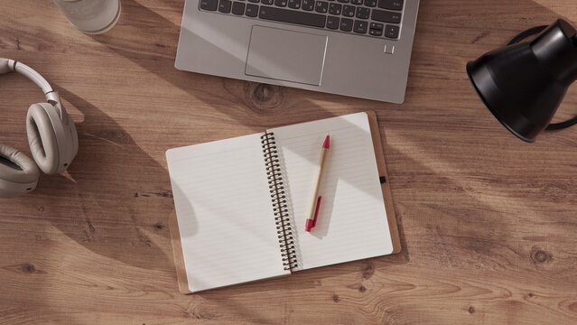 notebook with pen made of recyclable materials, cardboard, lies on desktop in office or home office next to laptop, headphones and table lamp. Preparation for online study, top down view.