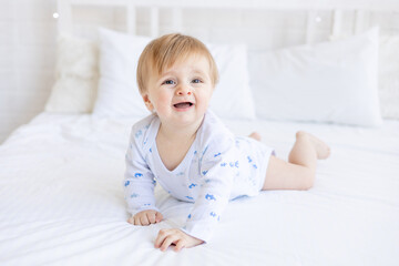 a capricious baby boy of six months blonde wants to sleep or cries on the crib lying on his stomach in a room at home with white cotton bedding, the concept of children's goods and accessories