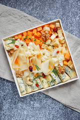 Assorted sorts of cheese on a wooden plate, grey background, top view