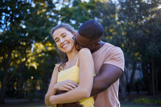 Couple, date in park with hug and outdoor in nature, love and commitment with interracial relationship. Trust, support and happy people, black man and woman smile on face with fresh air with partner