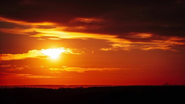 Timelapse dramatic sunset through soft clouds in the orange sky over the horizon. Big bright red sun with sunrays moves down. Awesome epic cloud space, vibrant color. Time Lapse. Sundown in Yellow Sky