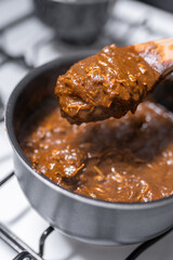 A young woman is cooking chicken with mole sauce using a gas stove