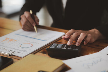 Businessman using a calculator to calculate numbers on a company's financial documents, he is analyzing historical financial data to plan how to grow the company. Financial concept.