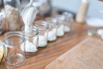 A young woman is pouring yogurt in a small jar