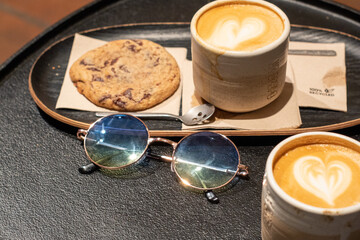 Café con leche y espuma con forma de corazón, con una cookie de avena y chocolate en una cafetería de Madrid descansando.