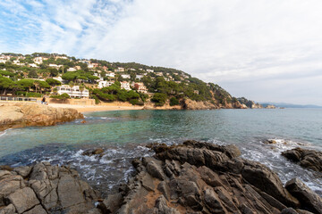 Paisaje marino de la costa brava con la imagen de la playa con la verde montaña al fondo y sus pequeñas casas entre los árboles con las vistas al mar.