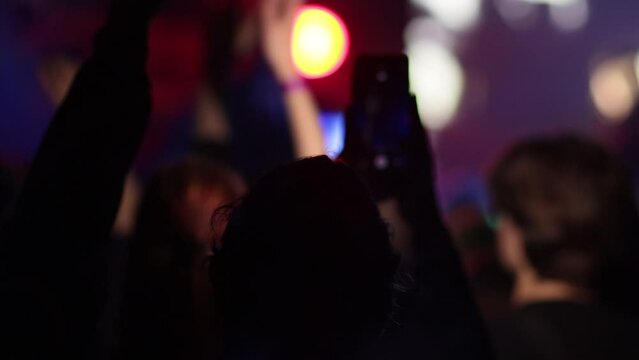 Fans Raise Hands and takes a photos in Front of Bright Colorful Strobing Lights on Stage. slow motion