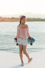 Teenager asian beautiful women surfskate or skateboard outdoors on beautiful summer day. happy young women play surf skate at park near the beach on morning time. Sport activity lifestyle concept.