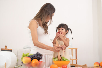 Mom with her two children eating fruits and vegetables. Mother with daughter having breakfast at home. Happy lifestyle family. Mother with her children in the kitchen cooking together.