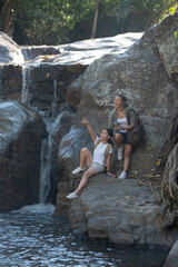 Female hiker looking at waterfall. Happy female backpacker enjoying amazing tropical waterfall raised hands travel lifestyle and success concept vacations into the wild nature on background mountain