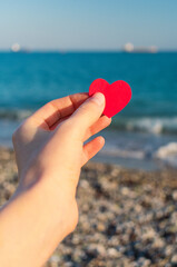 The red heart in the hand of the girl against the background of the sea horizon during sunset.