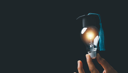 academy and success graduate education concept. businessman hand holding bright, electric light bulb with degree cap on black background. business education, knowledge, learning idea with copy space. - obrazy, fototapety, plakaty