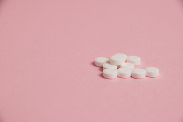 Many white pills on pink paper background with copy space