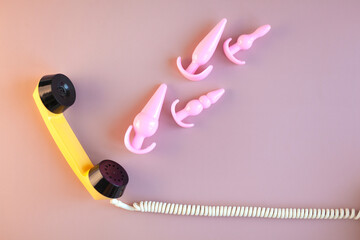 The handset of a yellow retro phone on a pink background. Pink sex toys come out of the phone tube. The concept of phone sex, ordering toys for adults. Banner with space for text - obrazy, fototapety, plakaty