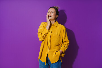 Young cheerful laughing girl wearing yellow shirt against purple background