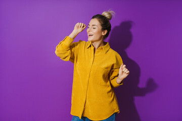 Young cheerful girl wearing yellow shirt dancing against purple background