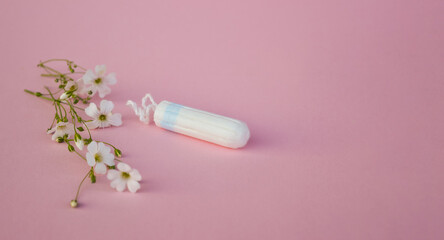The concept of careful and gentle protection in critical days. Menstruation period concept. Hygienic white tampons for women with flowers on pink backround.