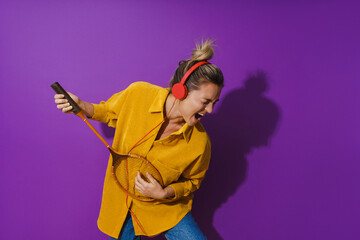Cheerful girl is jamming out in her yellow shirt while wearing red headphones. She's strumming away on her racket like it's a guitar.