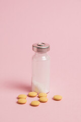 Ampoule and yellow pills on pink paper background with copy space. Concept of treatment of covid 19 and colds.