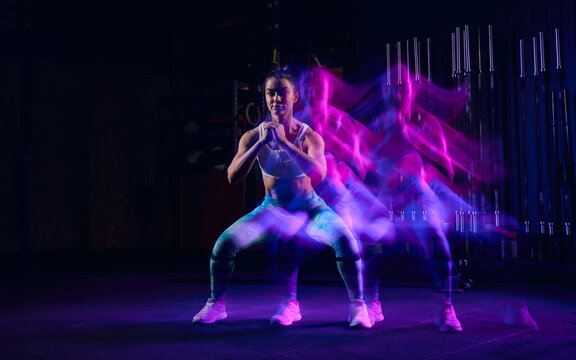 Workout at gym. Sportive woman in sportswear and sportsfoot training in modern fitness room over dark background with mixed neon light. Active and healthy lifestyle