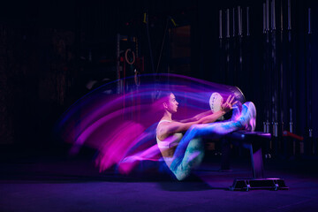 Workout at gym. Sportive woman in sportswear and sportsfoot training in modern fitness room over dark background with mixed neon light. Active and healthy lifestyle