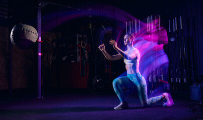 Workout at gym. Sportive woman in sportswear and sportsfoot training in modern fitness room over dark background with mixed neon light. Active and healthy lifestyle