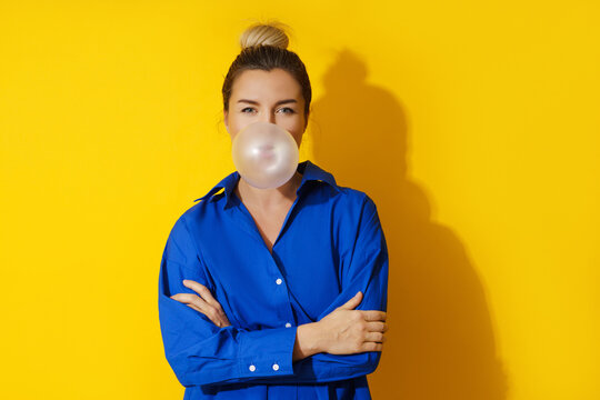 Happy woman blowing a bubble with chewing gum against yellow background