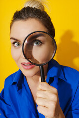 Curious woman is peering through magnifying glass with great interest, examining something closely