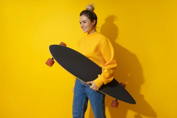 Poster Young cheerful girl with longboard against yellow background © blackday