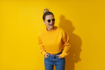 Young cheerful girl wearing yellow sweatshirt and sunglasses against yellow background