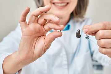 Hearing aid battery replacement. Positive audiologist showing hearing aid and battery for it,...
