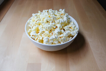 Popcorn snack in bowl on a light wood table. Pop corn ready to wath movie.