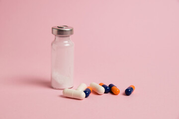 Multicolored medical capsules and ampoule on pink background with copy space