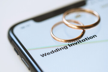Golden wedding rings on top of a smartphone and the text on the screen  - Wedding Invitation