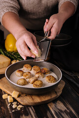 woman grating parmesan on meatballs in cream sauce