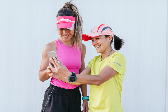 Two sporty girls looking at their smart phones. Smiling after exercising. LGBT couple