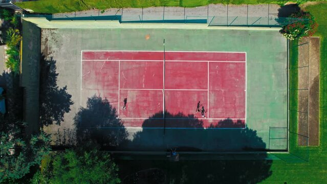 Top view of people playing tennis on the tennis court. New players enter the field. Summer club competition. Old paddle court and friends practicing moves. Drone top down view on court