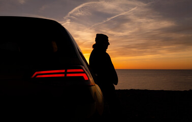 Silhouette of man with his car against sea and sky during sunset - Powered by Adobe