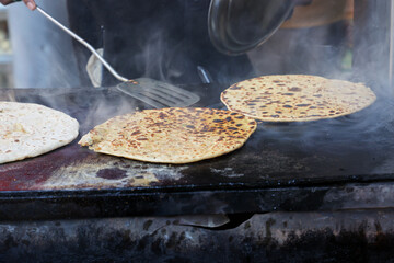 Making or cooking Aloo Paratha Indian potato stuffed flatbread with butter on top. Served with fresh sweet Lassi chutney and pickle. Street food in Kullu Manali Himachal Pradesh India.