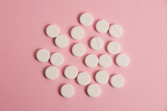 Flatlay, many white pills on a pink paper background